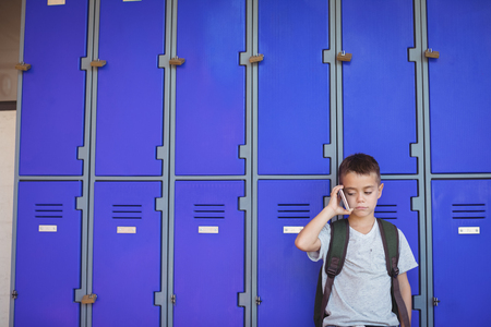 Boy talking on mobile phone while standing against lockers at schoolの写真素材