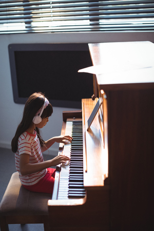 High angle side view of girl wearing headphones while practicing piano in classroom at music schoolの写真素材