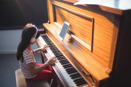 High angle view of concentrated girl wearing headphones while practicing piano in classroom at music schoolの写真素材