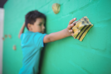 Boy reaching climbing holds on green wallの写真素材