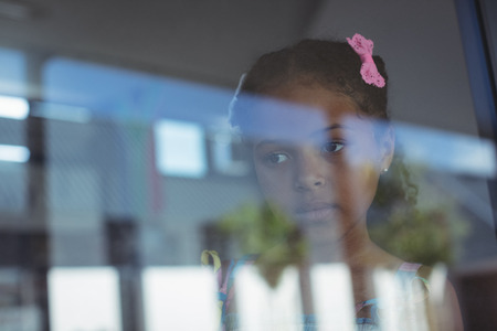 Contemplated girl seen through window glass of school