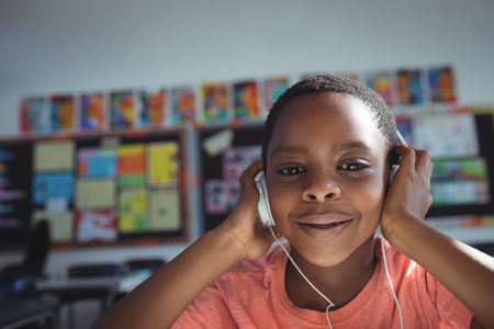 Close up portrait of boy listening music with headphones in classroomの写真素材