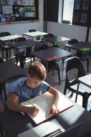 High angle view of boy writing in book by laptop at deskの写真素材