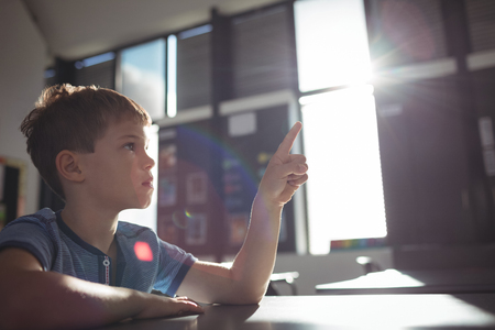 Boy pointing while sitting at desk in schoolの写真素材