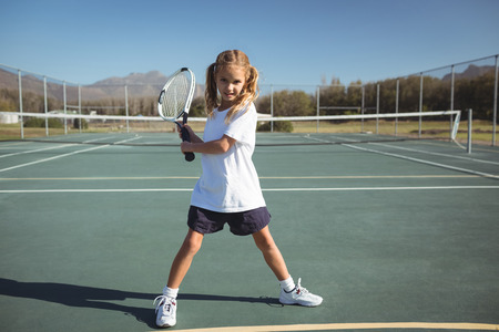 Full length of girl playing tennis on court during sunny dayの写真素材