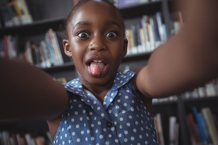 Portrait of happy girl making face against bookshelf in libraryの写真素材