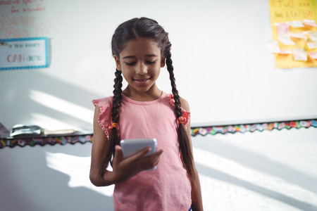 Girl using mobile phone while standing against wall in schoolの写真素材