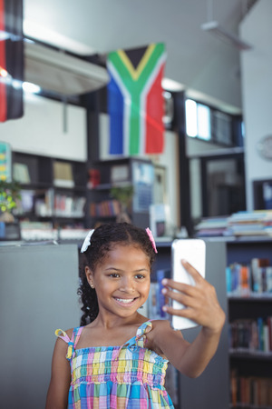 Smiling girl taking selfie while standing in libraryの写真素材