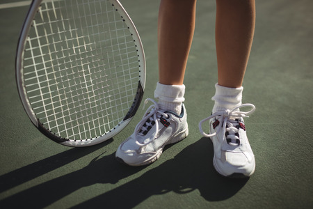 Low section of girl with tennis racket standing on courtの写真素材