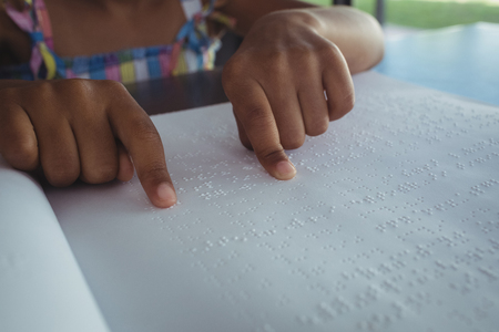 Cropped hands of girl reading braille at tableの写真素材