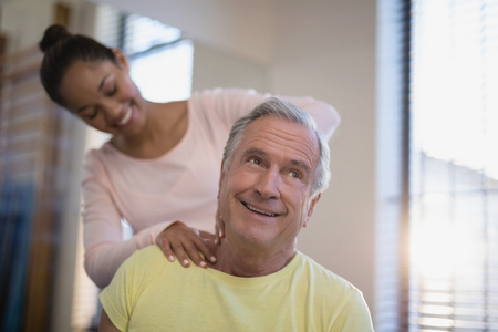 Smiling senior male patient receiving neck massage from therapist at hospital wardの写真素材