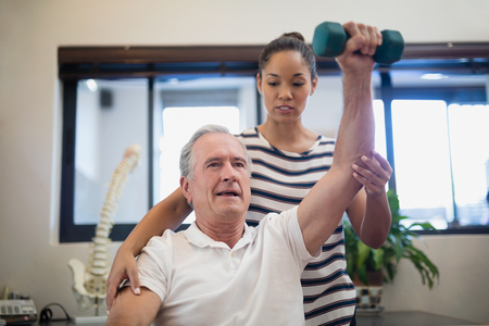 Female doctor looking at senior patient lifting dumbbell in hospital wardの写真素材