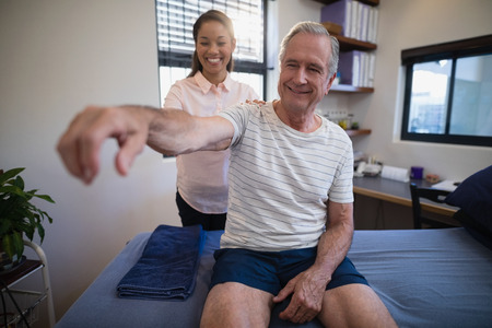 Smiling female doctor examining shoulder of senior male patient at hospital wardの写真素材