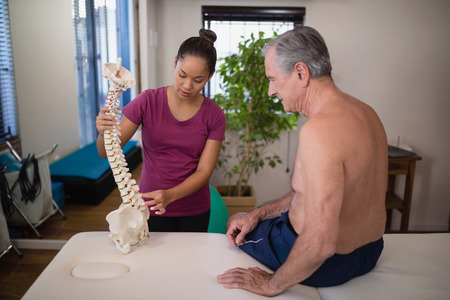 Female therapist explaining shirtless senior male patient with artificial spine at hospital wardの写真素材