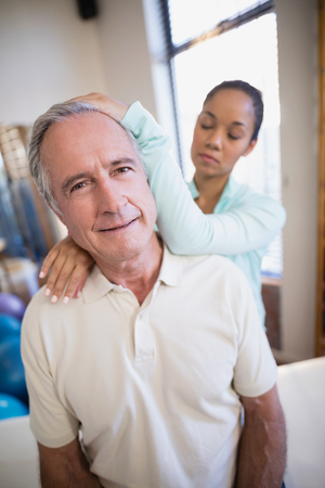 Portrait of senior male patient receiving neck massage from female therapist at hospital wardの写真素材
