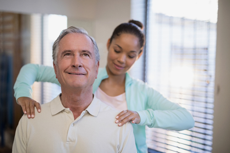 Young female therapist giving shoulder massage to senior patient at hospital wardの写真素材