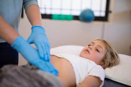 Boy getting stomach examination from female therapist at hospital wardの写真素材