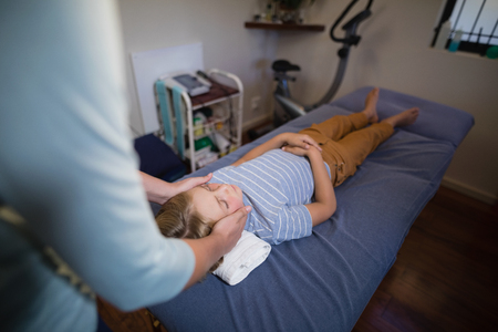 High angle view of female physiotherapist giving head massage to boy lying on bed at hospital wardの写真素材