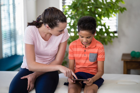 Boy looking while female therapist pointing at digital tablet at hospital wardの写真素材