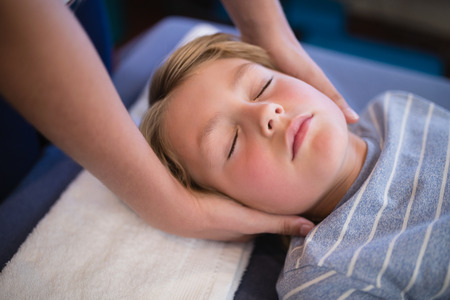 High angle view of boy with eyes closed receiving neck massage from female therapist at hospital wardの写真素材