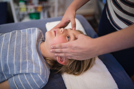 Midsection of female therapist giving head massage to boy lying on bed at hospital wardの写真素材