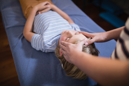 High angle view of female therapist giving head massage to boy at hospital wardの写真素材