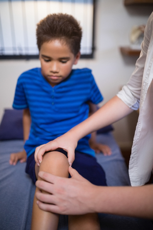 Boy looking while female therapist massaging knee at hospital wardの写真素材