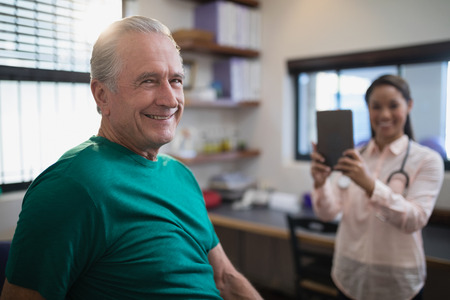 Portrait of smiling senior male patient with female therapist holding digital tablet at hospital wardの写真素材
