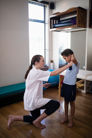 Side view of female therapist kneeling while examining boy at hospital wardの写真素材