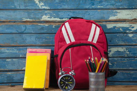 Bagpack, books, alarm clock and pen holder against blue wooden backgroundの写真素材