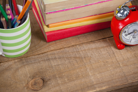 Stack of books, alarm clock and pen holder on wooden backgroundの写真素材