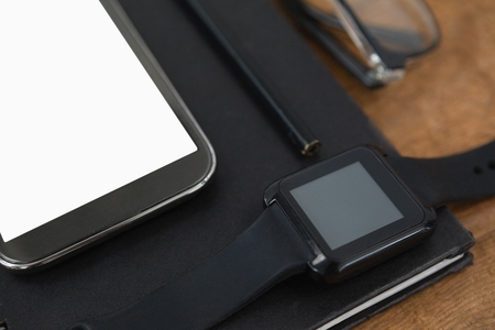 Close-up of diary, smart watch, pencil, smartphone and spectacles on wooden backgroundの写真素材