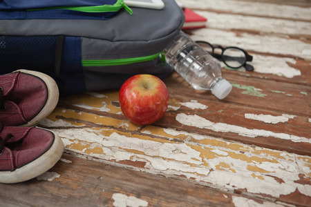 Bagpack, water bottle, apple, shoes and spectacle on wooden backgroundの写真素材