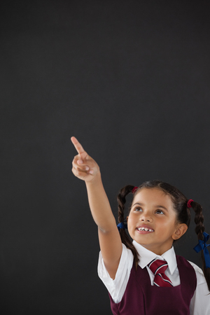Smiling schoolgirl pointing against blackboard in classroomの写真素材