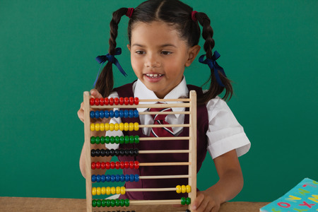 Schoolgirl using abacus against chalkboard in classroomの写真素材