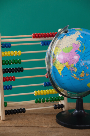 Globe and abacus on wooden table against green backgroundの写真素材