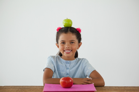 Portrait of schoolgirl sitting with green apple on her head against white backgroundの写真素材