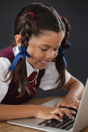 Adorable schoolgirl using laptop against blackboard in classroomの写真素材