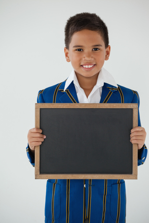 Portrait of schoolboy holding blank writing slate against white backgroundの写真素材