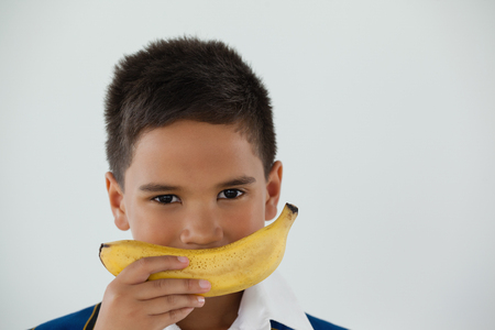 Portrait of schoolboy holding banana against white backgroundの写真素材