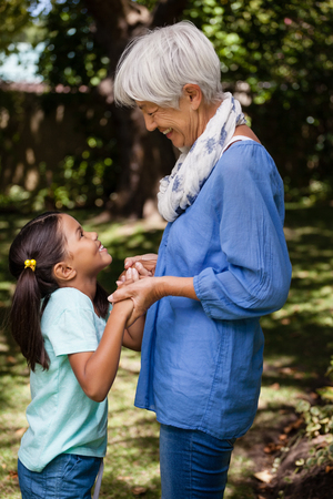 Side view of grandmother and daughter standing while holding hands at backyardの写真素材