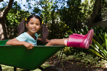 Side view of girl sitting on wheelbarrow at backyardの写真素材