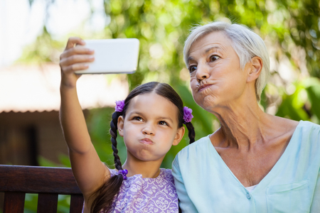 Girl and grandmother making faces while taking selfie at backyardの写真素材