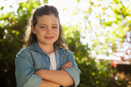 Portrait of confident girl with arms crossed standing against plants in backyardの写真素材