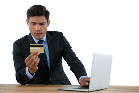 Businessman holding credit card while using laptop at table against white backgroundの写真素材