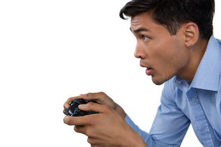 Side view of young businessman making face while playing video game against white background