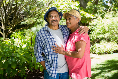 Portrait of senior couple standing with arm around in garden on a sunny dayの写真素材
