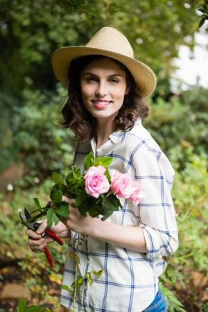 Portrait of woman trimming flowers with pruning shears in garden on a sunny day