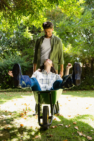 Man interacting with woman while pushing wheelbarrow in garden on a sunny dayの写真素材