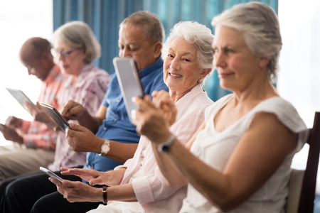 Senior people sitting on chairs while using digital tablets at retirement homeの写真素材